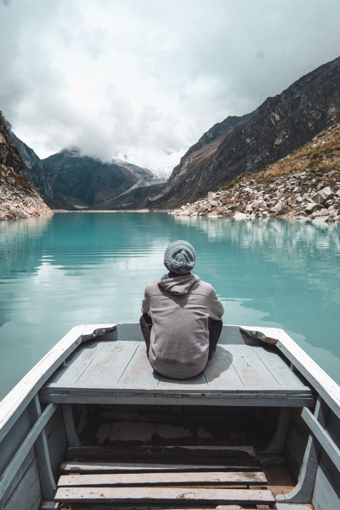 Contemplative view of a person on a boat in a serene lake surrounded by mountains in Huaraz, Peru.